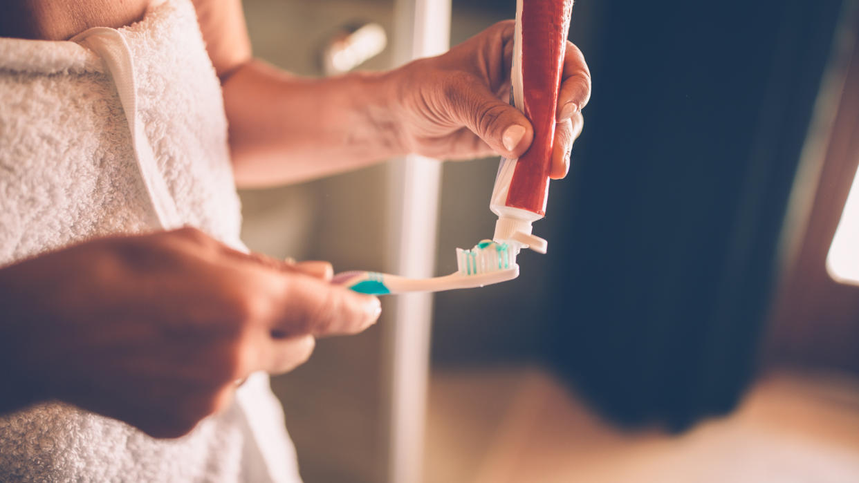 Close-up of senior woman's hands squeezing and applying toothpaste on toothbrush to brush her teeth.