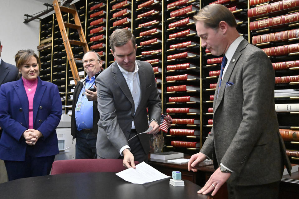 Kentucky Governor Andy Beshear, center, and Lt. Governor Jacqueline Coleman, left, present the paperwork to Secretary of State Michael Adams to officially enter the race for reelection in Frankfort, Ky., Monday, Dec. 5, 2022. (AP Photo/Timothy D. Easley)