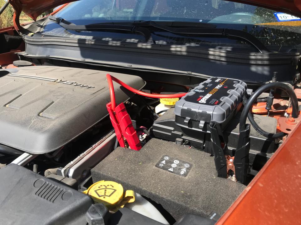 Under a hood, a jump starter batter hooked up to a car