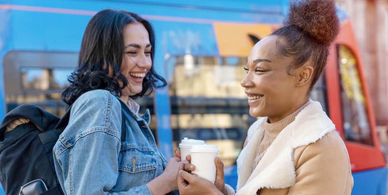 two women in a denim jacket is talking to each other , drinking coffee and waiting for a tram at the stop lifestyle photo