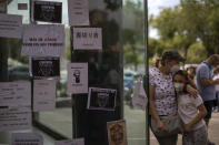 A woman and her daughter stand next to the window of a a car dealerships covered by leaflets during a protest in Barcelona, Spain, Friday, May 29, 2020. Employees in Spain of Japanese giant Nissan took to the streets for the second day in a row to protest the closure of three Barcelona plants as the carmaker scales down its global production. Hundreds of workers have surrounded at least four of Nissan's car dealerships on Friday in or around the northeastern city, covering their windows with leaflets reading "Nissan betrays 25,000 families" and "We will keep fighting" among others. (AP Photo/Emilio Morenatti)