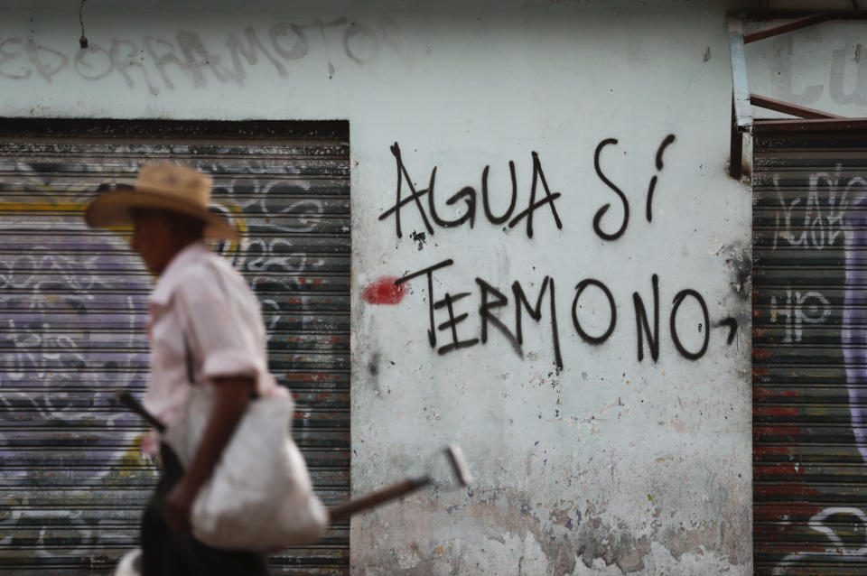 A farmer walks past graffiti that reads in Spanish "Water yes, Termo no," in San Pedro Apatlaco, Morelos state, Mexico, Saturday, Feb. 22, 2020. Dozens of mostly indigenous communities along the 159 kilometers of pipeline have united to fight a mega-project they believe will deprive them of water for their crops, while contaminating the soil and air. (AP Photo/Eduardo Verdugo)