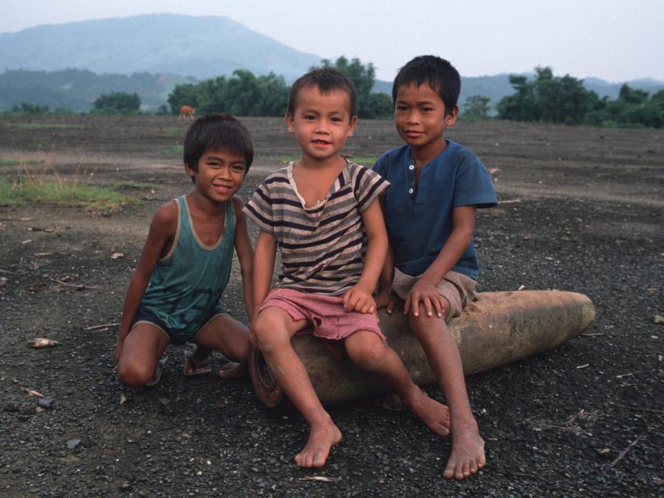 Kids in Vang Vieng, Laos pose for a photo while sitting on a disarmed US bomb dropped during the Vietnam War.