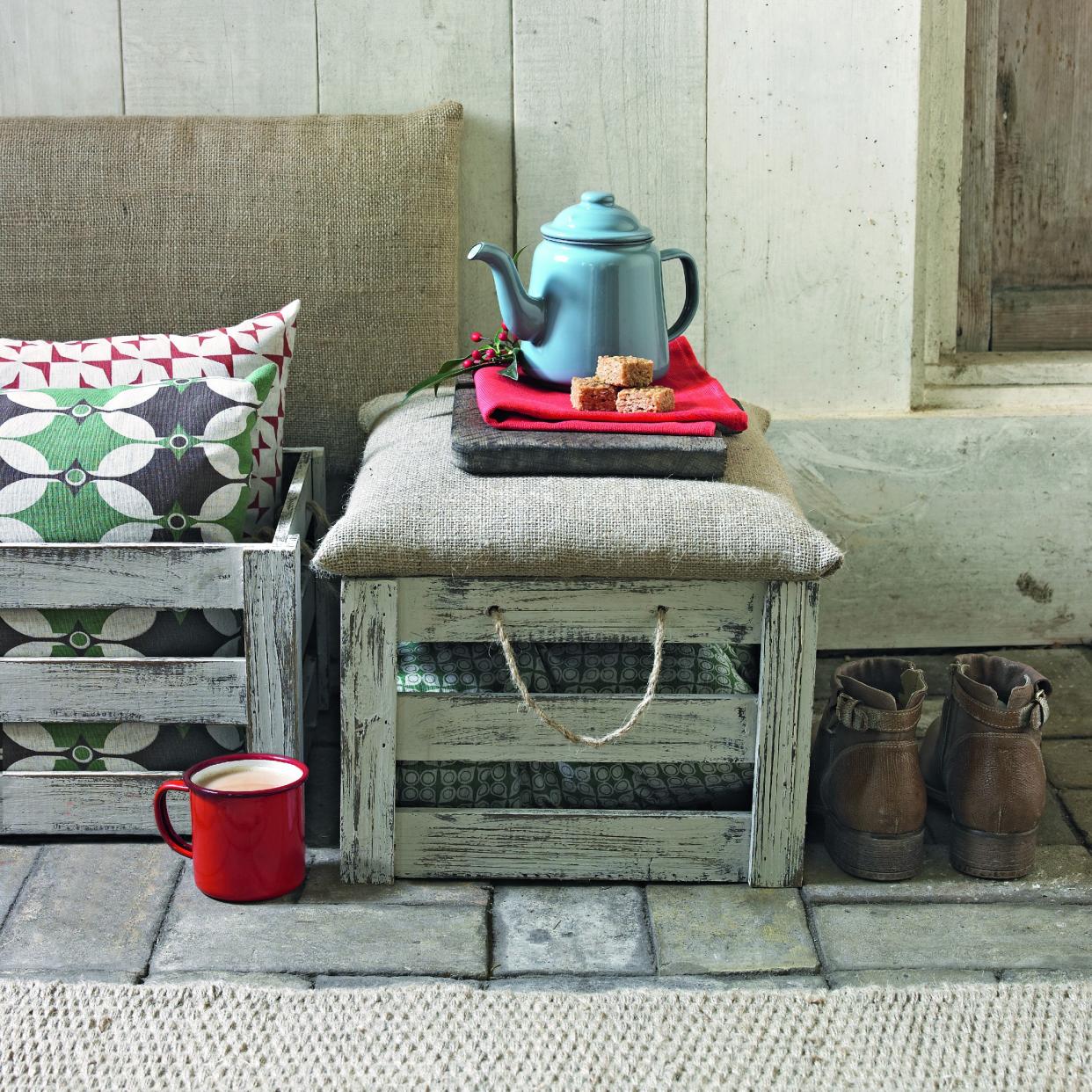  An ourdoor bench made from wooden crates with a teapot on top and a tea cup next to it. 