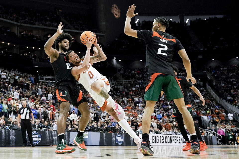 Texas forward Timmy Allen drives to the basket between Miami forward Norchad Omier, left, and guard Isaiah Wong in the first half of an Elite 8 college basketball game in the Midwest Regional of the NCAA Tournament Sunday, March 26, 2023, in Kansas City, Mo. (AP Photo/Charlie Riedel)