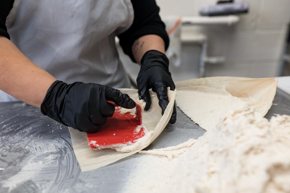 Patricia Nora, an employee at Food City Supermarket in El Paso spreads masa on the corn husk for the tamales on Tuesday, Dec. 19, 2023.