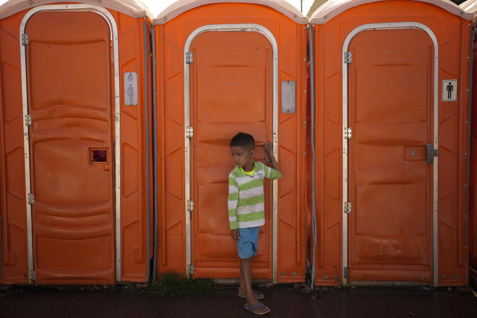 The son of Venezuelan migrant Maria Rodriguez waits outside a portable toilet outside an NGO-run shelter for migrants as they wait for visas to legally enter Brazil, in Pacaraima, Brazil, on the border with Venezuela, Thursday, April 6, 2023. The Rodriguez family said they closed their unprofitable cheese-making business this year and decided to join other relatives in the southern state of Paraná, where the men in the family planned to work in construction. (AP Photo/Matias Delacroix)