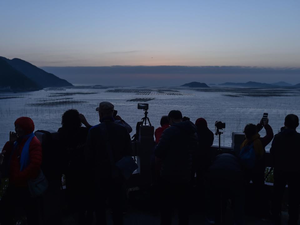 A crowd of Chinese tourists with tripods and cameras watch a sunrise at the Niu Yu mud flat in Xiapu.