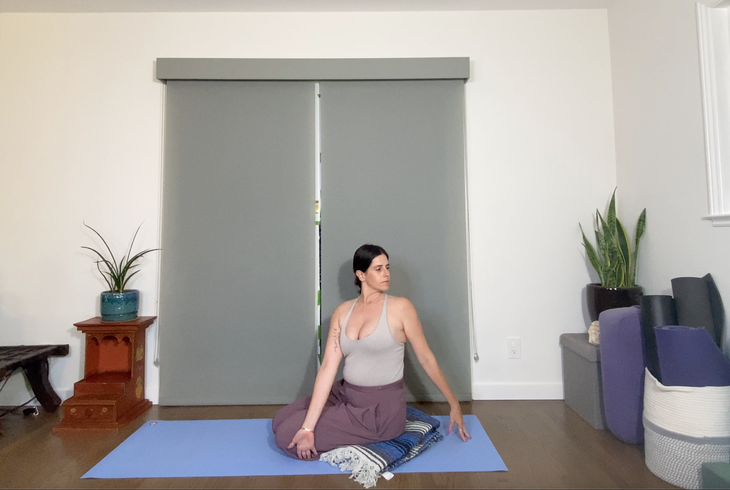 A woman in purple pants and a gray tank practices Bharadvajasana.