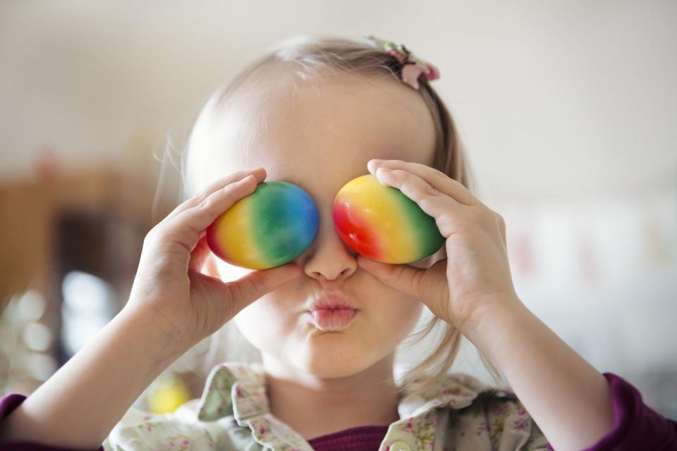 child holding colorful painted eggs over eyes