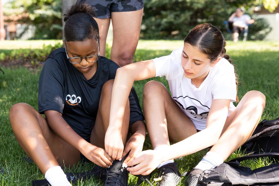 Sutton Hull, of Park City, right, helps Aliyah Bugingo, of Democratic Republic of Congo, tie her brace before their #SheBelongs soccer practice at Lone Peak Park in Sandy on Thursday, July 6, 2023. #SheBelongs is a four-month program bringing together refugee and nonrefugee girls through soccer. | Megan Nielsen, Deseret News