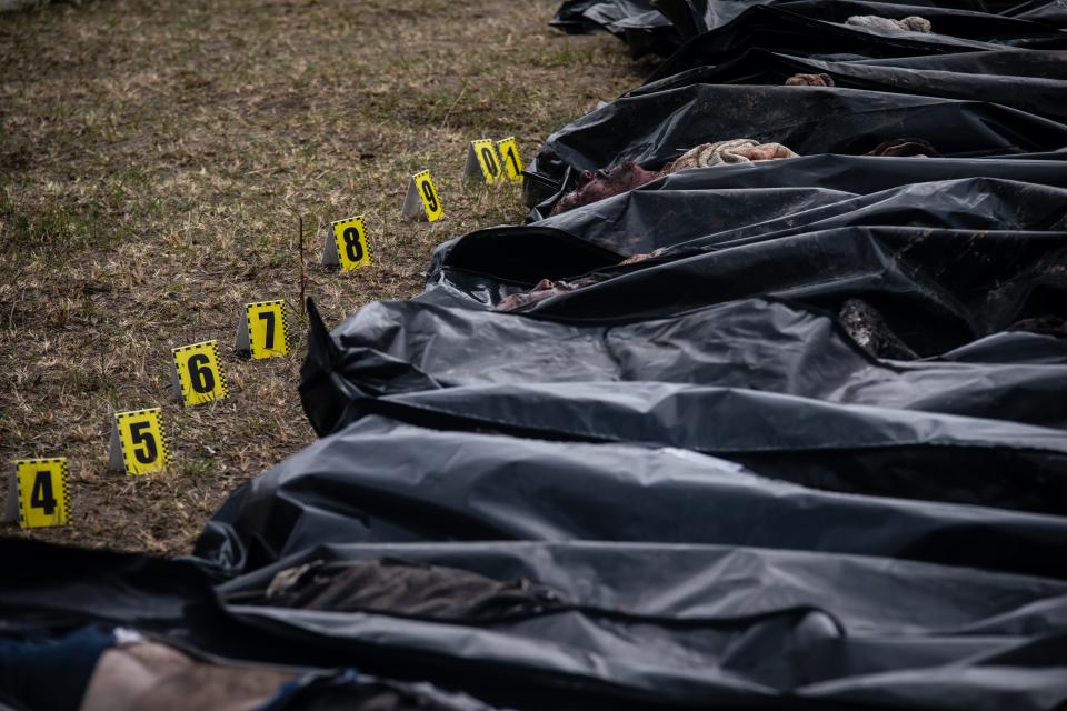 A row of bodies are enclosed in bags next to yellow, numbered labels.