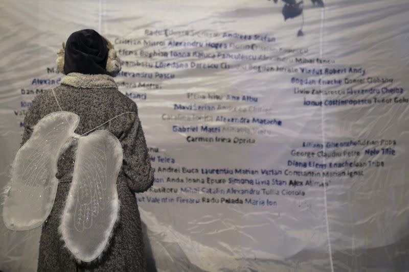 A girl wearing angel wings looks at a poster that features the names of the 65 people that died during or in the aftermath of the fire at Colectiv Club on October 30, 2015, during an event that commemorated the victims