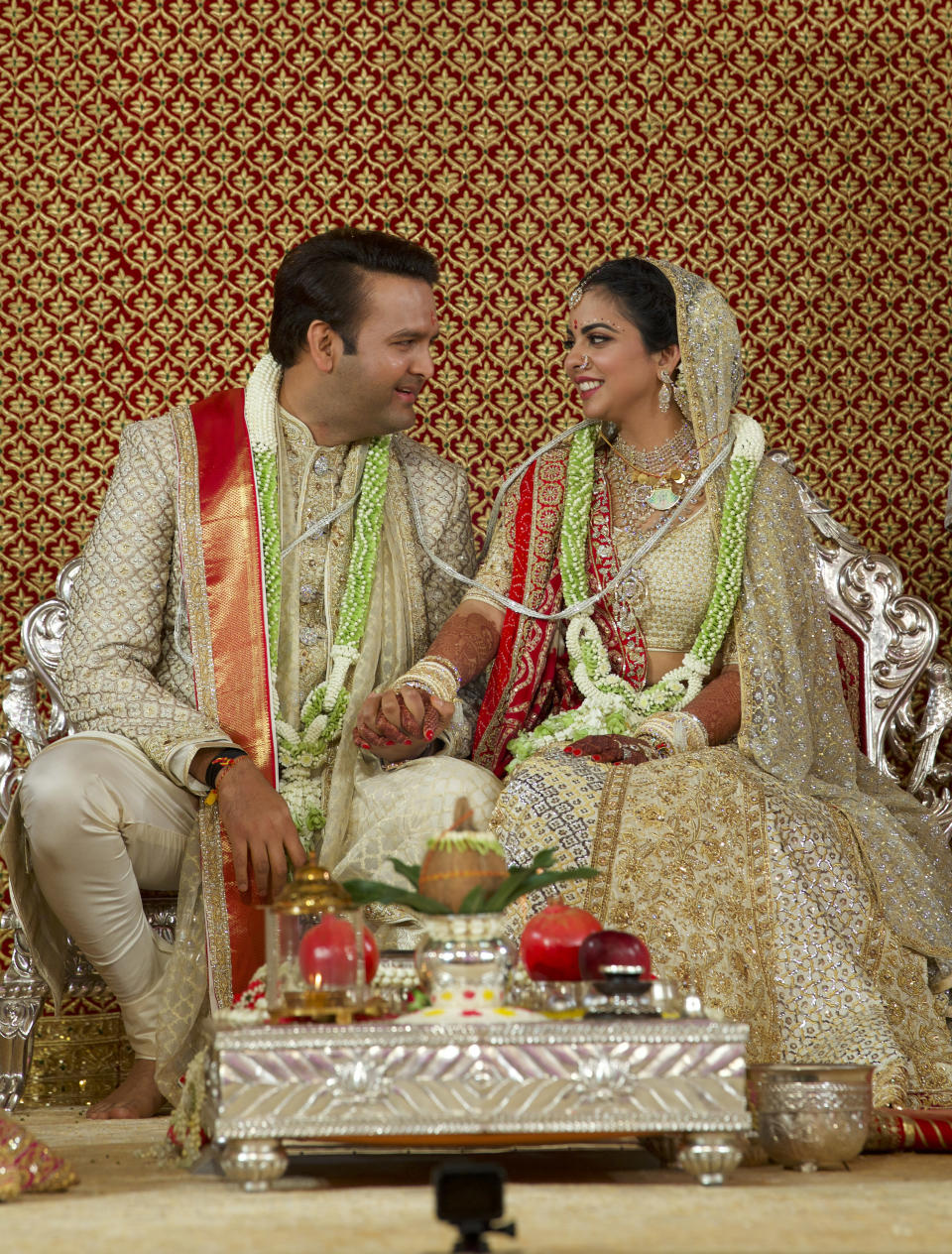 In this handout photo released by Reliance Industries Limited, newlyweds Isha Ambani, right, and Anand Piramal sit holding hands in Mumbai, India. In a season of big Indian weddings, the Wednesday marriage of the scions of two billionaire families might be the biggest of them all. Isha is the Ivy League-educated daughter of industrialist Mukesh Ambani, thought to be India's richest man. The groom is the son of industrialist Ajay Piramal, thought to be worth $10 billion. (Reliance Industries Limited via AP)
