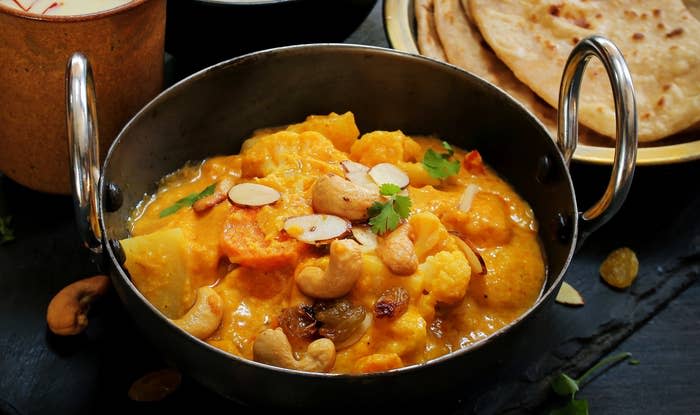A bowl of creamy navratan korma, garnished with almonds and coriander and served with parathas