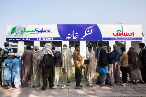 Workers line up outside a free communal kitchen for a meal - Credit: Saiyna Bashir