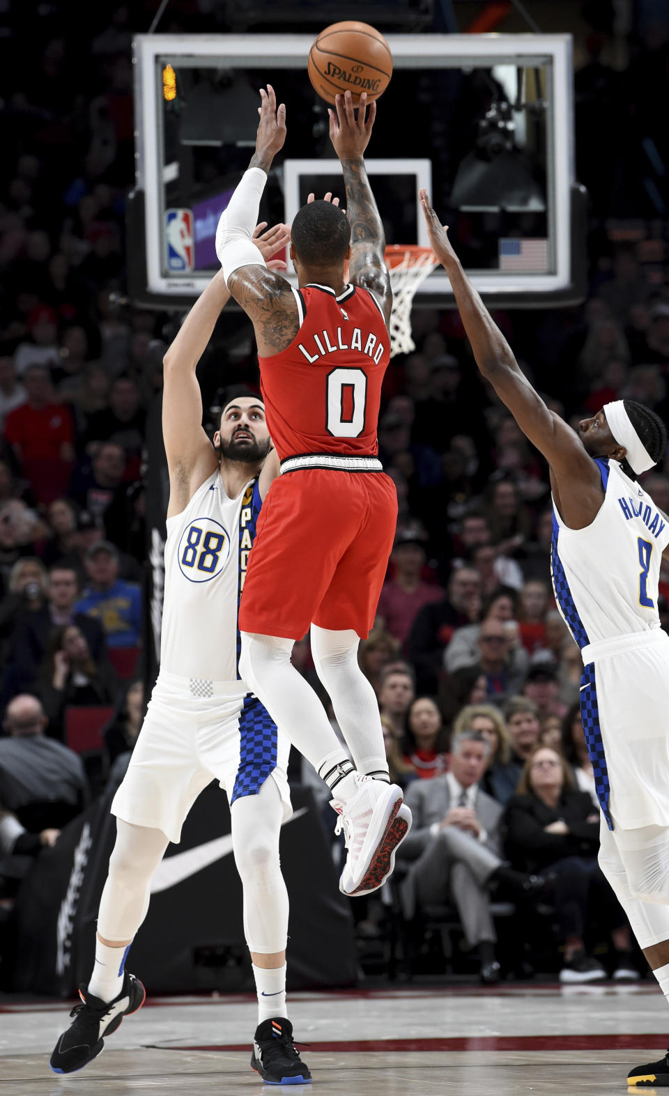 Portland Trail Blazers guard Damian Lillard, center, hits a shot over Indiana Pacers center Goga Bitadze, left, and Indiana Pacers forward Justin Holiday, right, during the first half of an NBA basketball game in Portland, Ore., Sunday, Jan. 26, 2020. (AP Photo/Steve Dykes)
