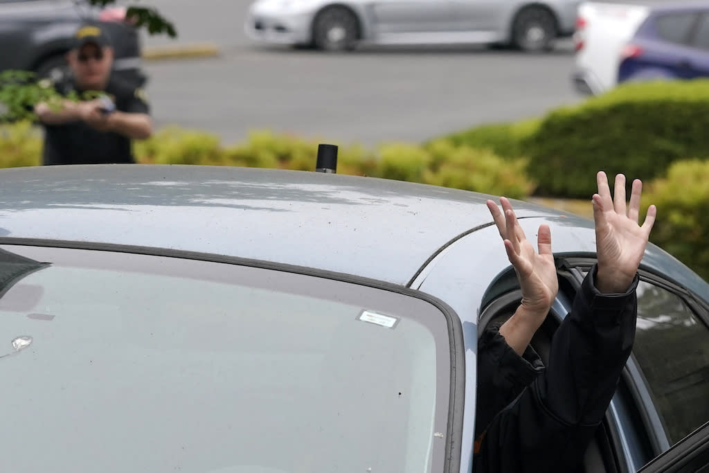 Two hands poking out of a car door as a police officer points a gun