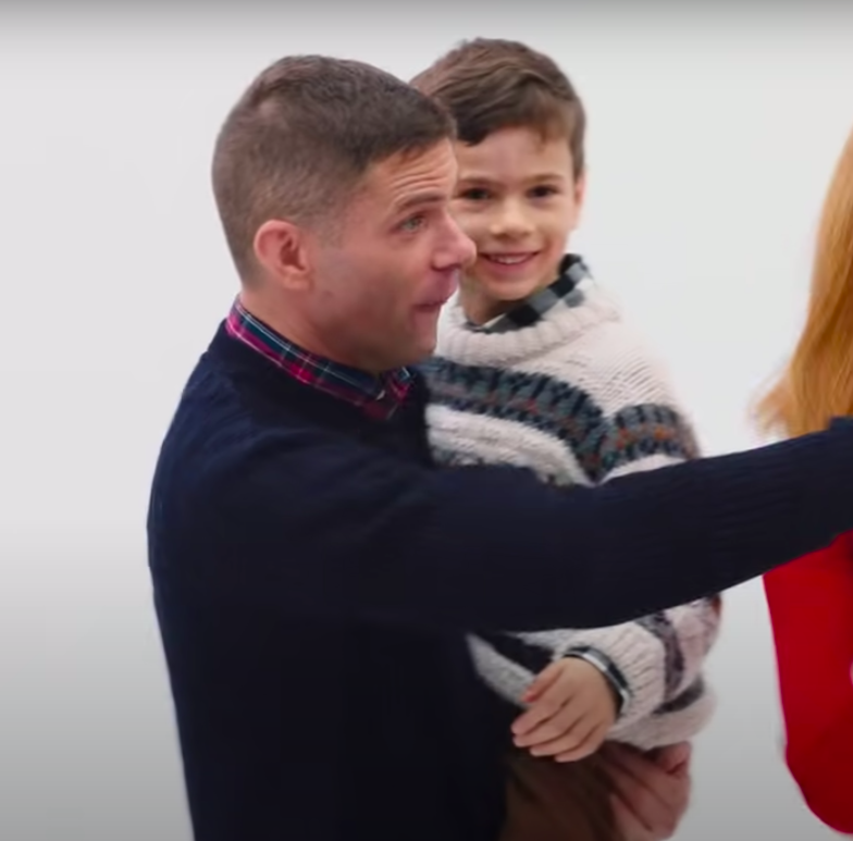 Mikey holds his son, who's wearing an itchy Christmas sweater