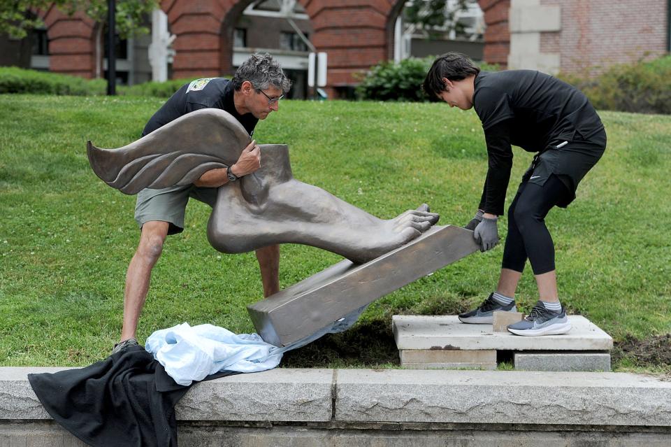 Sculptor Michael Alfano, left, of Hopkinton, with his assistant, Yerzat Tleulin, install Winged Foot, one of 20 sculptures in the "Of Many Minds" waterfront sculpture exhibit at the Charlestown Navy Yard on June 16. The exhibit runs through December 2023.