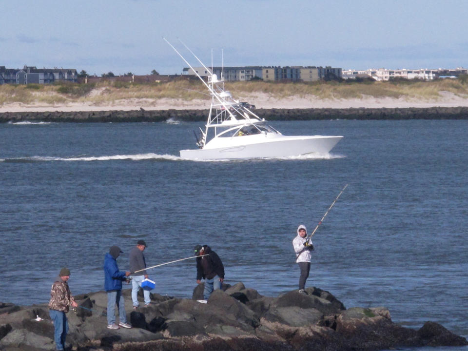This Oct. 18, 2019 photo shows anglers fishing from a jetty as a large boat sails by in Atlantic City, N.J. On Oct. 22, 2019, a conference at Monmouth University in West Long Branch, N.J. examined growing competition for space out on the ocean by users including the fishing, shipping, wind energy industries and conservationists. (AP Photo/Wayne Parry)