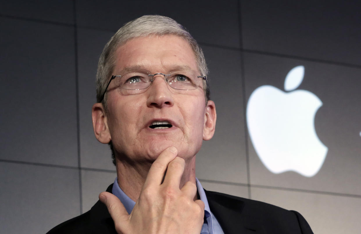 Apple CEO Tim Cook puts his hand to his chin while answering a question with the Apple logo in the background.