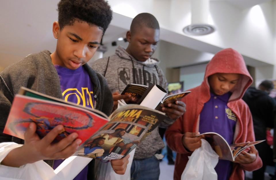 Boys, shopping bags in hand, stand while poring over comic books.