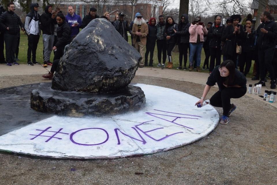 Albion College junior Azu Davaa-Ochir sprays “#ONEALBION” on the base of the campus rock during the unity demonstration on April 11, 2019. The gathering was in response to a series of alleged racial harassment incidents on campus targeting the school's Black and Asian population.