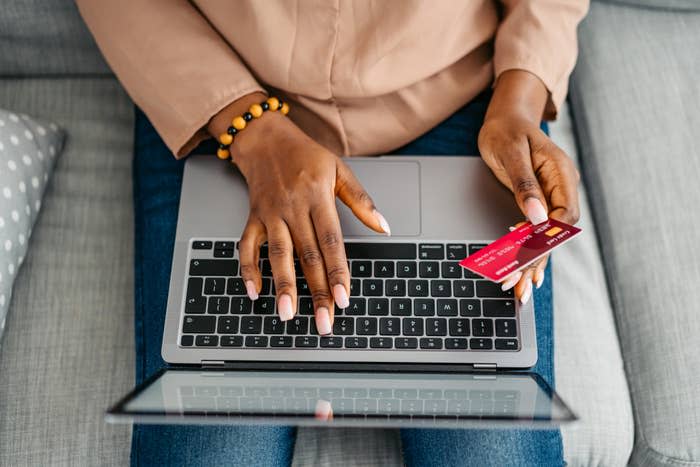 Person holding a credit card is typing on a laptop keyboard while sitting on a couch, suggesting online shopping or online banking activities