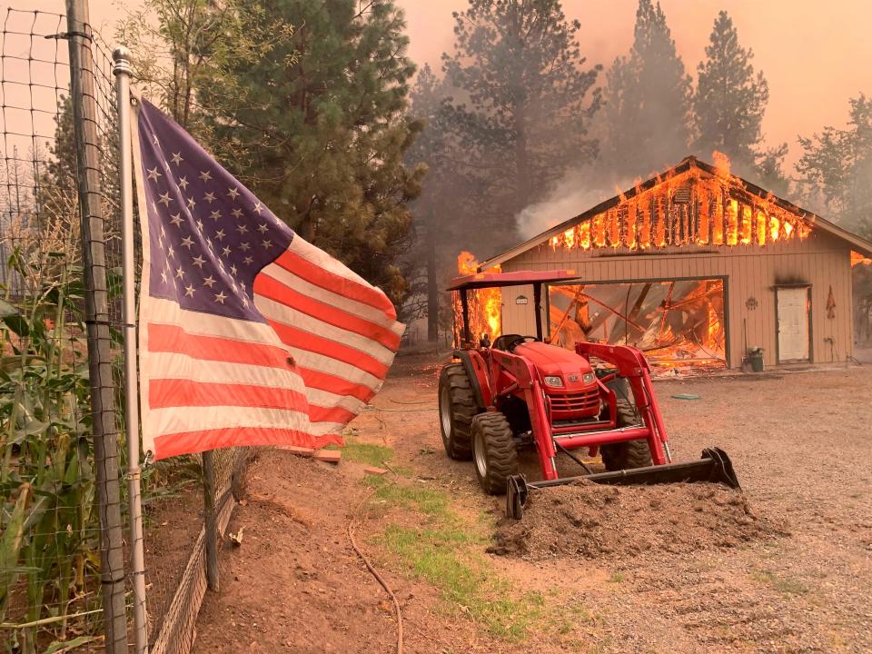 A red tractor is left behind as a home burns outside of Taylorsville in Plumas County on Friday, Aug. 13, 2021.