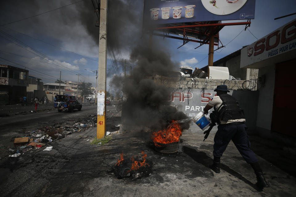 A policeman throws water on burning tires after they were dragged out of the road to break up a barricade in Port-au-Prince, Haiti, Wednesday, Oct. 2, 2019. A group of men was protesting at the intersection after commissioning a mural of opposition organizer Jose Mano Victorieux, known as "Badou," who they said was executed Saturday night by unknown assailants.(AP Photo/Rebecca Blackwell)