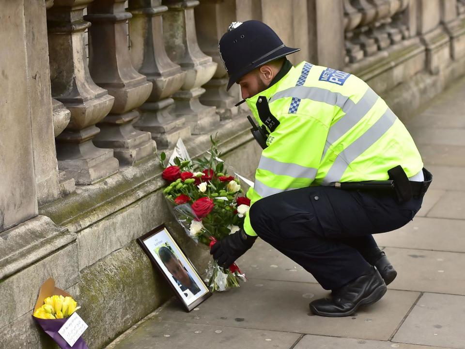 A police officer places flowers and a photo of PC Keith Palmer on Whitehall near the Houses of Parliament (PA)