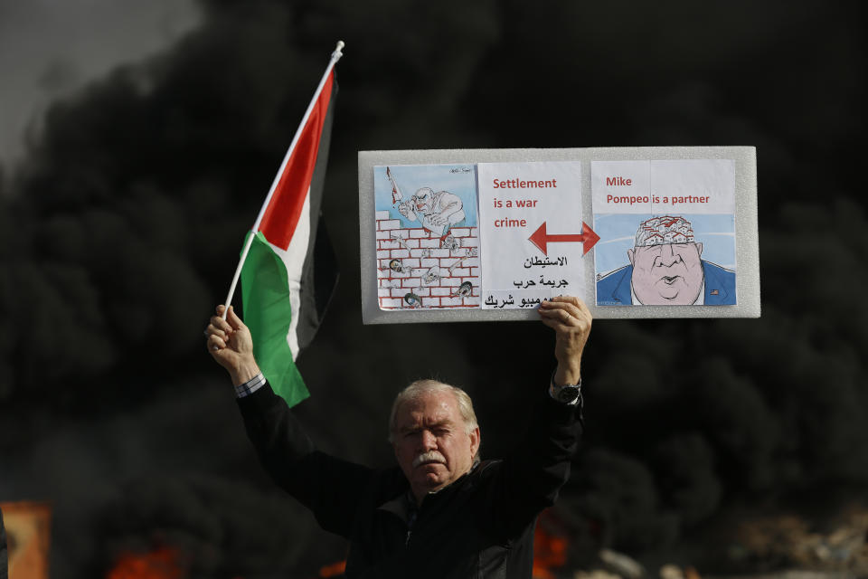 Palestinian hold poster depicting Israeli Prime Minister Benjamin Netanyahu, left, and US Secretary of State Mike Pompeo as clashes with Israeli troops broke out during the protest against the U.S. announcement that it no longer believes Israeli settlements violate international law., at checkpoint Beit El near the West Bank city of Ramallah, Tuesday, Nov. 26, 2019, (AP Photo/Majdi Mohammed)