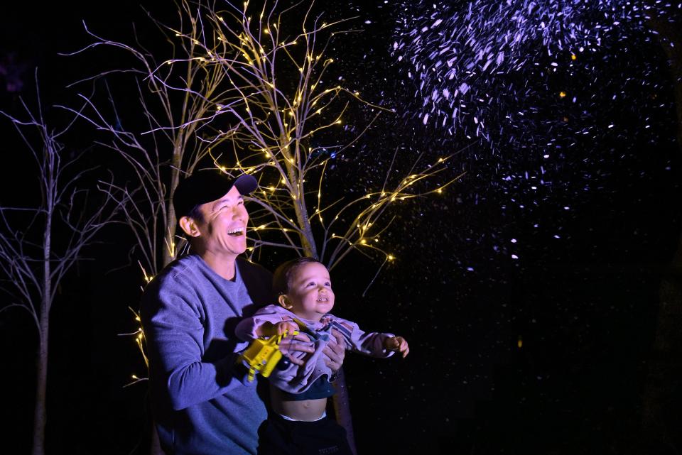 Thomas Matthews holds his almost 2-year-old son up to enjoy the fake snow being created along one of the walkways that are part of the Jacksonville Arboretum and Botanical Gardens "Dazzling Nights" event that transforms the grounds for the holidays.