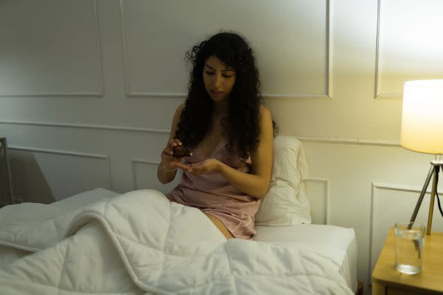 <p>Antonio_Diaz / Getty Images</p> Young female in pink pajamas taking medicine or vitamins before bed at night