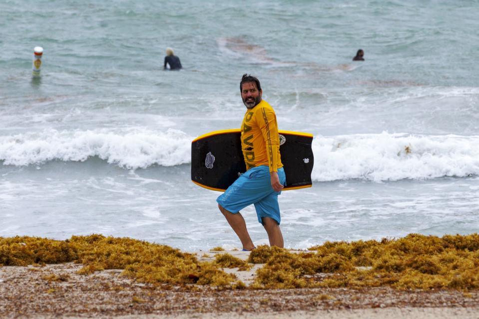 A surfer walks at the Bal Harbour Lighthouse on Wednesday, April 12, 2023, in Bal Harbour, Fla. According to the National Weather Service, rip current risk remains in effect until Thursday evening. (David Santiago/Miami Herald via AP)