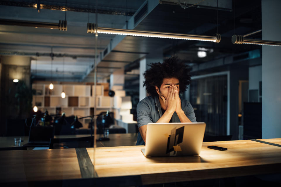 Tired businessman working late on laptop while sitting at illuminated desk in office