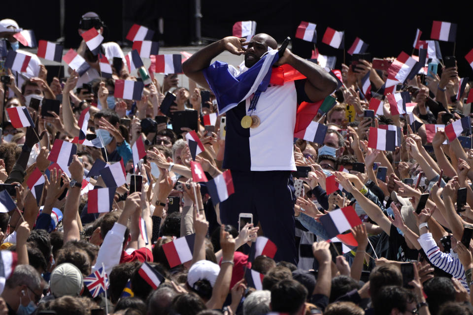 French Olympic heavyweight bronze medallist and mixed team gold medallist in Judoka, Teddy Riner, center, is wrapped in a French flag as he cheers on fans in the Olympics fan zone at Trocadero Gardens in front of the Eiffel Tower in Paris, Sunday, Aug. 8, 2021. A giant flag will be unfurled on the Eiffel Tower in Paris Sunday as part of the handover ceremony of Tokyo 2020 to Paris 2024, as Paris will be the next Summer Games host in 2024. The passing of the hosting baton will be split between the Olympic Stadium in Tokyo and a public party and concert in Paris. (AP Photo/Francois Mori)