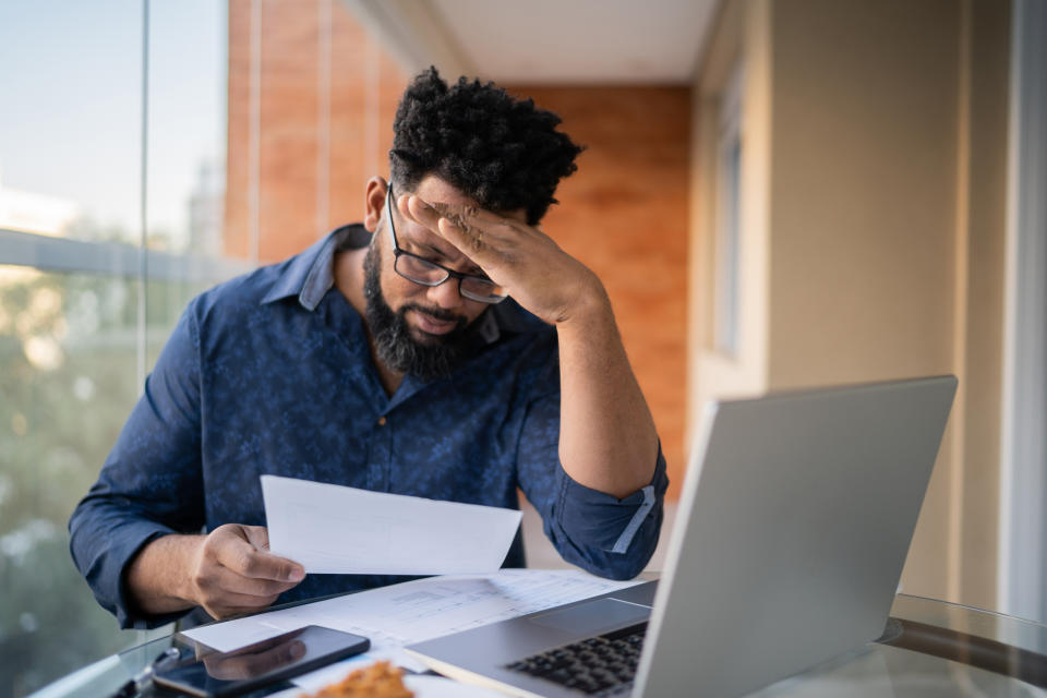 Man at a laptop reviews documents, expressing concern or concentration, possibly planning travel