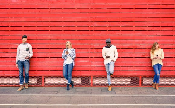 Four young people using smartphones standing against a red wall.