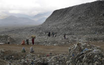 In this Tuesday, Dec. 11, 2018 photo people who scavenge recyclable materials from garbage for a living walk near a mountain of garbage at the dump on the outskirts of Kabul, Afghanistan. (AP Photo/Massoud Hossaini)