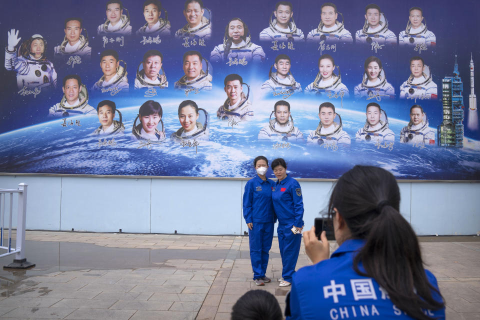 Staff members pose for a photo in front of a billboard depicting Chinese astronauts at the Jiuquan Satellite Launch Center in northwest China on Monday, May 29, 2023. China's space program plans to land astronauts on the moon before 2030, a top official with the country's space program said Monday. (AP Photo/Mark Schiefelbein)