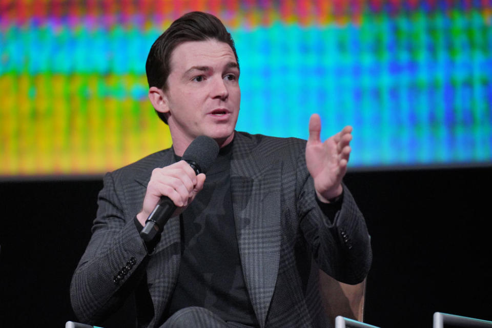 Man in a pinstripe suit speaking into a microphone at an event