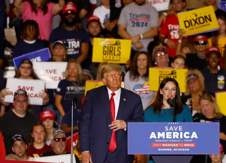 Former President Donald Trump looks on listening to Michigan Republican candidate for governor Tudor Dixon talk to the crowd after he invited her up on stage during his speech at the Macomb Community College, Sports and Expo Center in Warren on Saturday, October 1, 2022. Trump is heading back to Michigan for a campaign event on April 2.