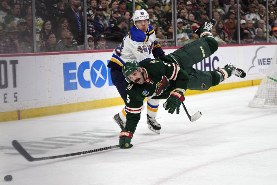 Minnesota Wild defenseman Jake Middleton (5) falls while reaching for the puck against St. Louis Blues right wing Kasperi Kapanen during the second period of an NHL hockey game, Saturday, April 8, 2023, in St. Paul, Minn. (AP Photo/Abbie Parr)