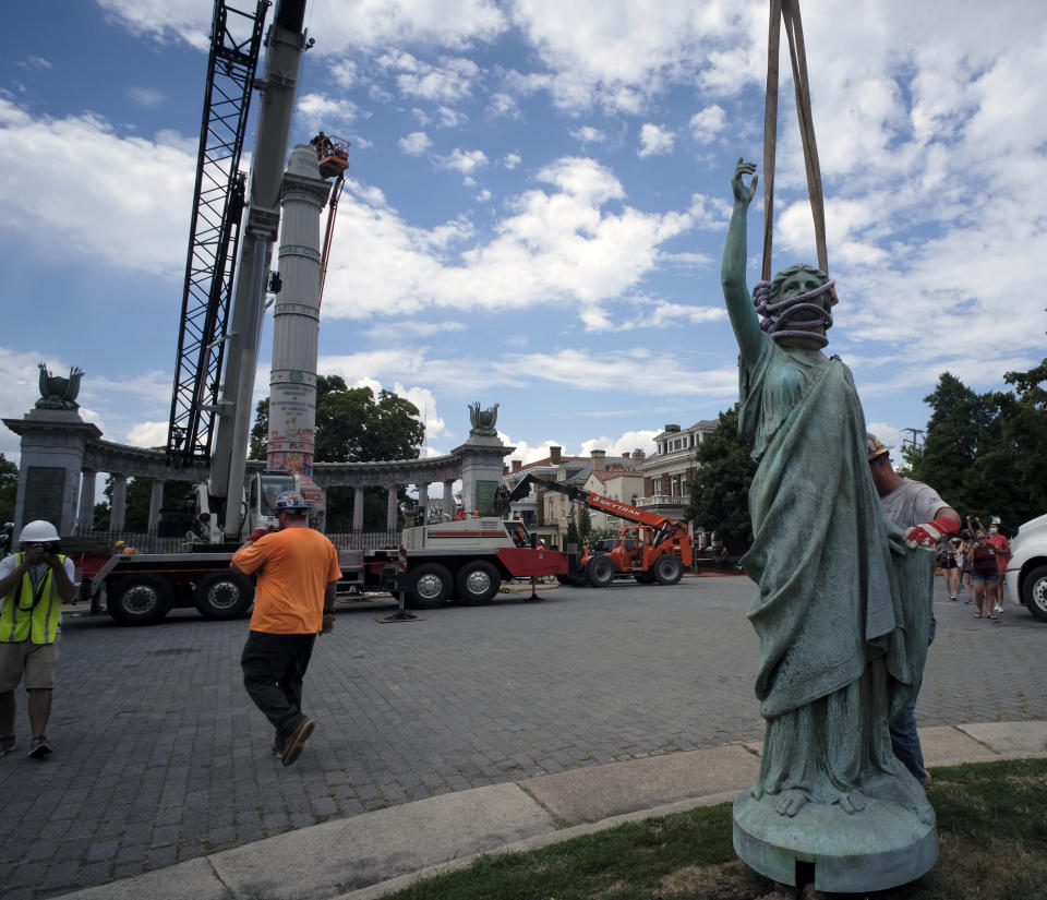 The statue from the Jefferson Davis monument, background, stands on the median after it was removed from its pedestal on Monument Ave. in Richmond, Va., Wednesday, July 8, 2020. The figure was atop a 65 foot tall Doric column topped by a bronze figure called "Vindicatrix," also known as "Miss Confederacy," is the work of Edward Virginius Valentine. (Bob Brown/Richmond Times-Dispatch via AP)