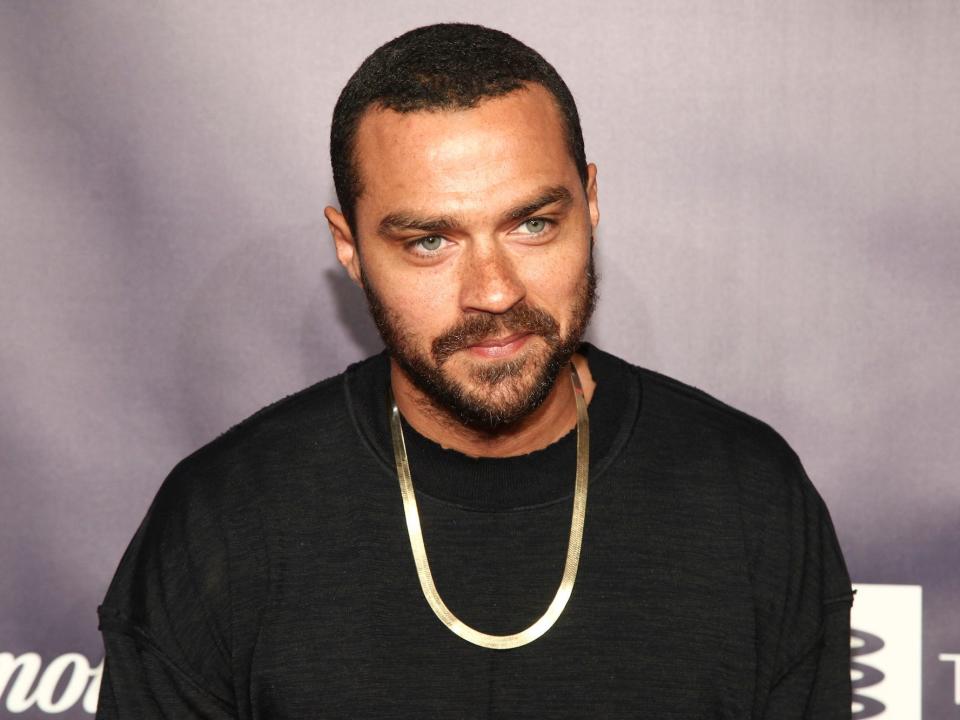 Jesse Williams wears a black shirt and silver chain.