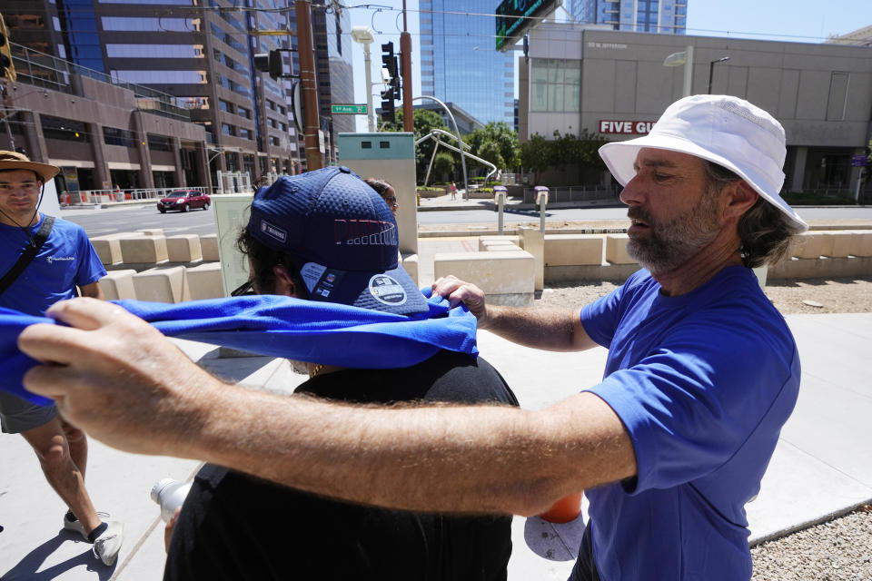 City of Phoenix Heat Response Program team volunteer David Coughenour, right, puts a cooling towel on a person as temperatures are expected to hit 119-degrees (48.3 Celsius) Thursday, July 20, 2023, in Phoenix. (AP Photo/Ross D. Franklin)