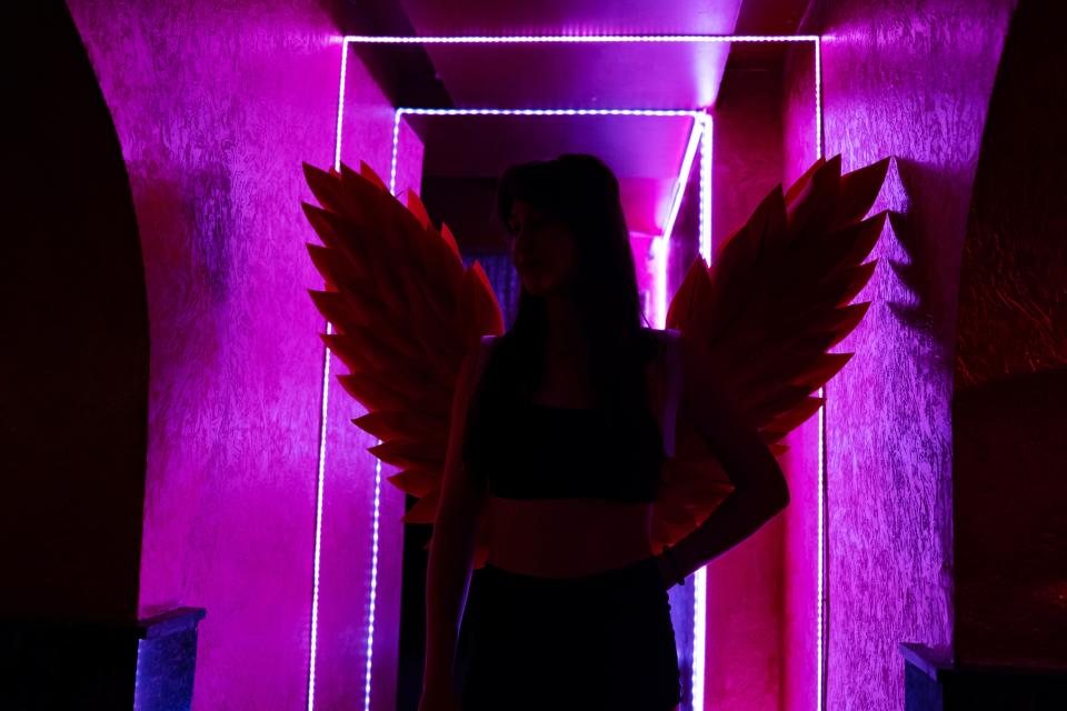 Woman wearing angle wings with purple light beaming through the back.