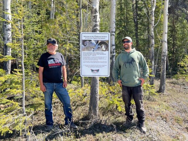 Danny Cresswell, left, and Adam Winters of the Carcross/Tagish First Nation at a sign for hikers at the base of Needles Mountain in the Yukon&#39;s Wheaton River Valley. (Maria Tobin/CBC - image credit)